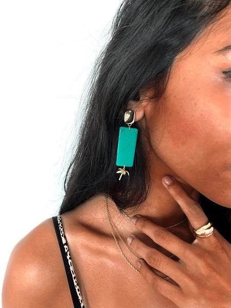 tan woman wearing jade green Polymer clay handmade earrings with gold plated silver earring post and palm tree pendant 